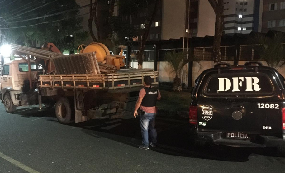 Policial civil ao lado de viatura, averiguando material na carroceria de um caminhão