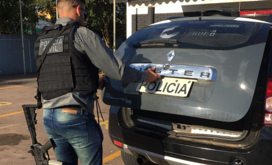 Policial civil abrindo tampa do porta-malas do carro para retirar suspeito