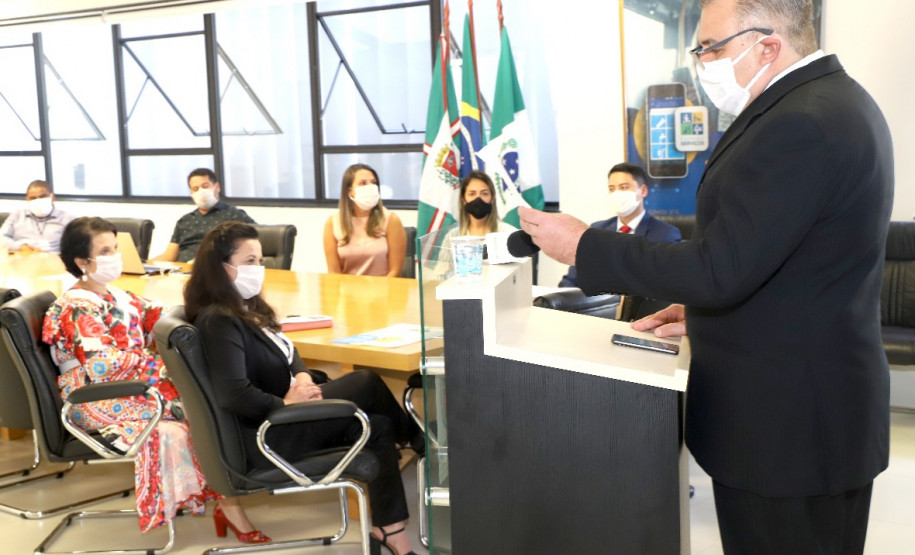 Participantes reunidos à mesa, enquanto uma pessoa, no púlpito, apresenta o material