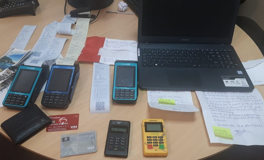 Máquinas de cartão, notebook, cartões de crédito e outros materiais sobre uma mesa.