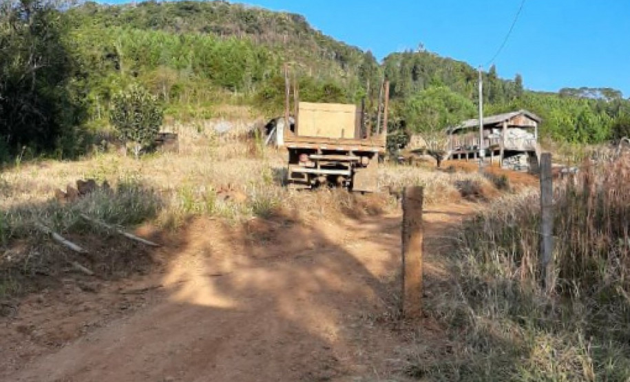 Estrada de terra cercada por vegetação, com um caminhão e uma construção