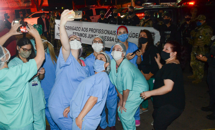 Profissionais da saúde fazendo selfie em frente à faixa da Polícia Civil