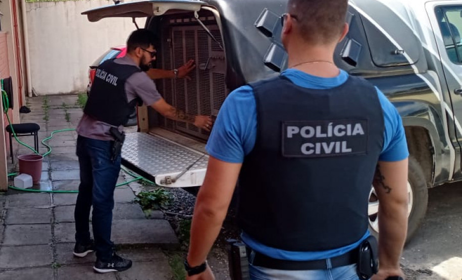 Dois policiais civis em pé, no momento em que retiram suspeito de viatura