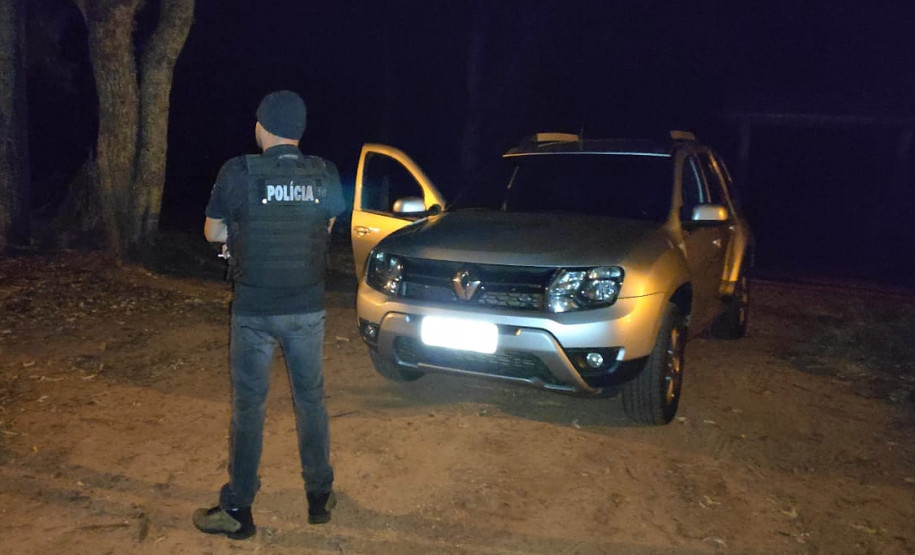 Policial civil ao lado de viatura descaracterizada, à noite