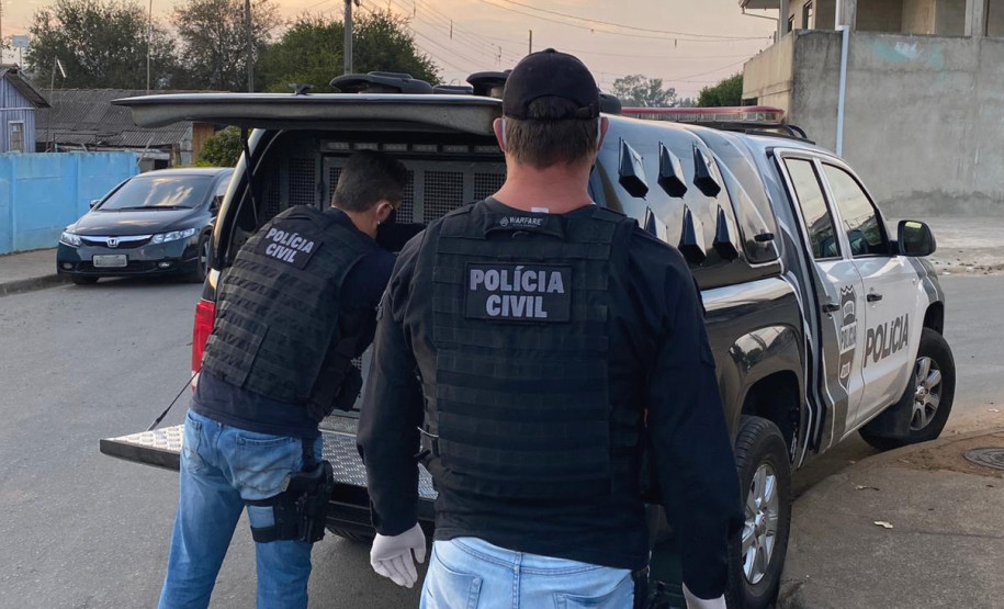 Dois policiais civis atrás de uma viatura com a tampa do porta-malas aberta