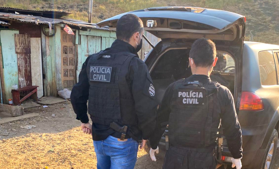 Dois policiais civis atrás de uma viatura com a tampa do porta-malas aberta