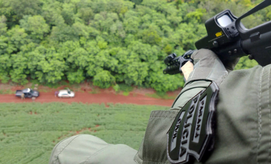 Policial civil no interior de helicóptero apontando arma para baixo