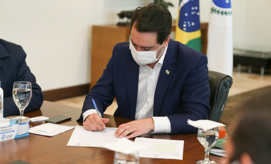 Governador sentado à mesa, assinando documento