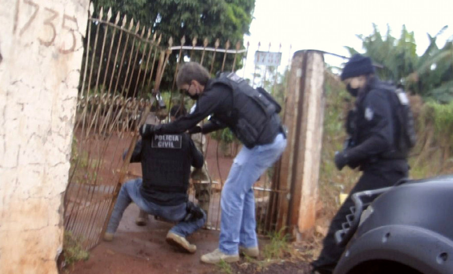 Policiais civis arrombando portão para entrar em residência de suspeito