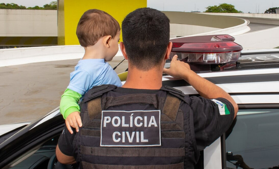 Policial civil segurando criança no colo, mostrando giroflex de viatura