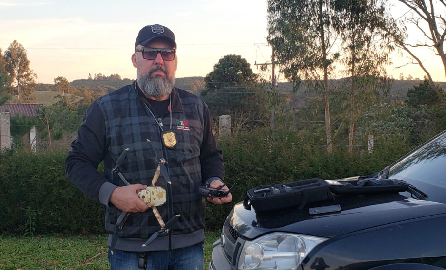 Investigador Fabiano Teixeira segurando drone ao lado de veículo
