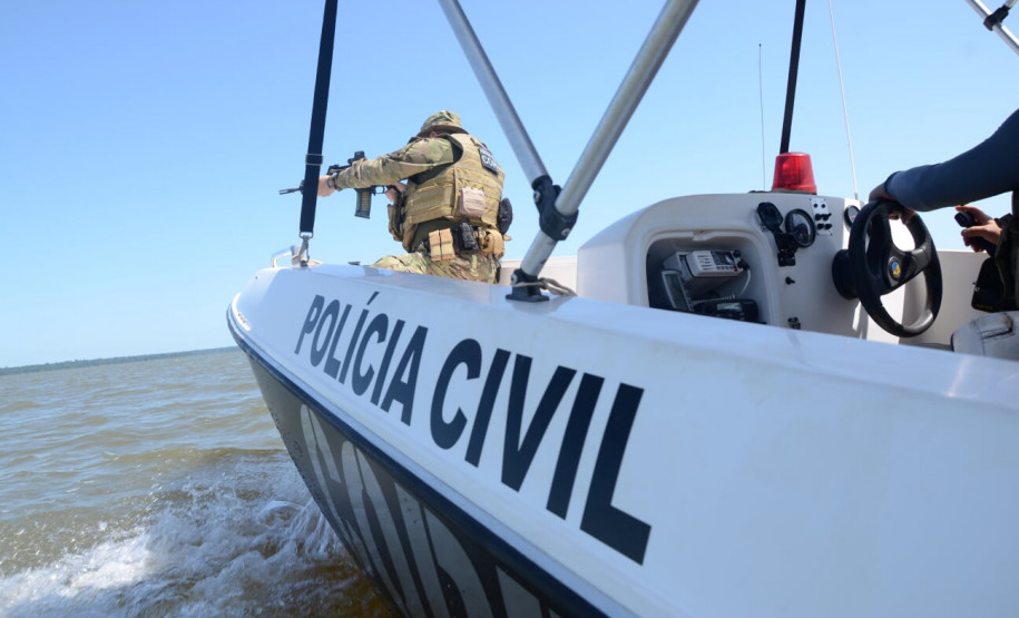 Policial civil na proa do barco da polícia civil, apontando arma