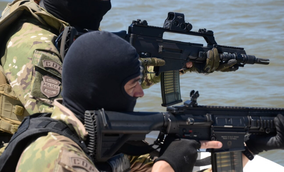 Dois policiais civis na proa do barco, apontando armas