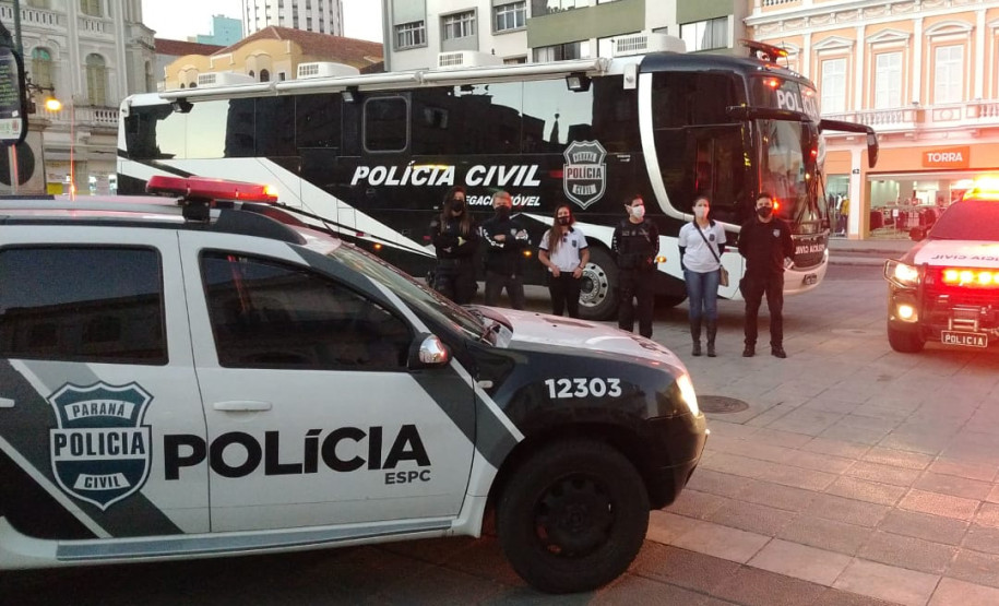 Policiais civis posando para foto entre viaturas e ônibus da PCPR