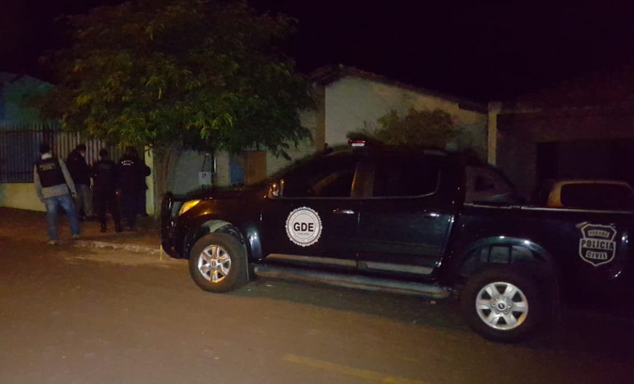Policiais entrando um uma residência. Ao lado, viatura estacionada.