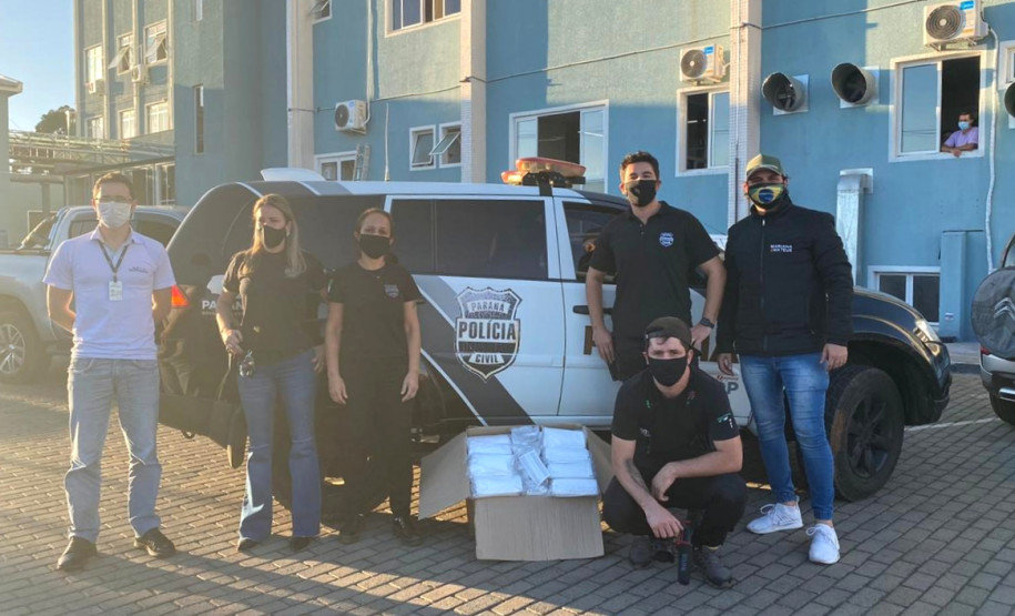 Policiais civis com caixa com máscaras, junto a viatura