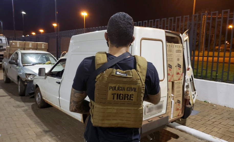 Policial civil em primeiro plano, de costas. Em segundo plano, veículos apreendidos