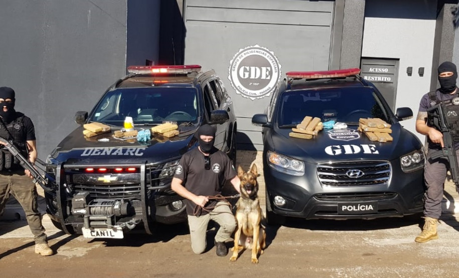 Policiais civis aparecem em frente à delegacia com cão policial e material apreendido