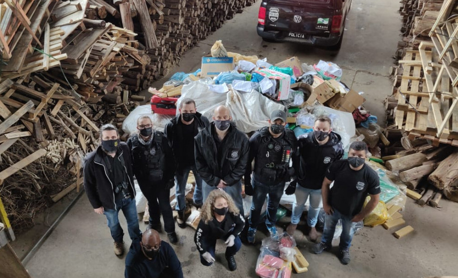 Policiais civis posam para foto, ao lado de pacotes de droga