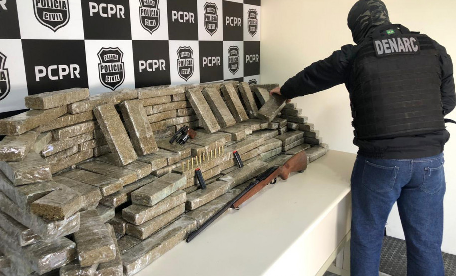 Policial civil empilhando tabletes de droga, sobre uma mesa