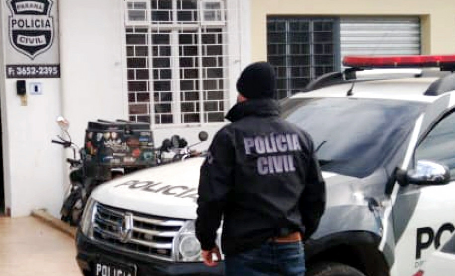 Policial civil ao lado de viatura, em frente à delegacia