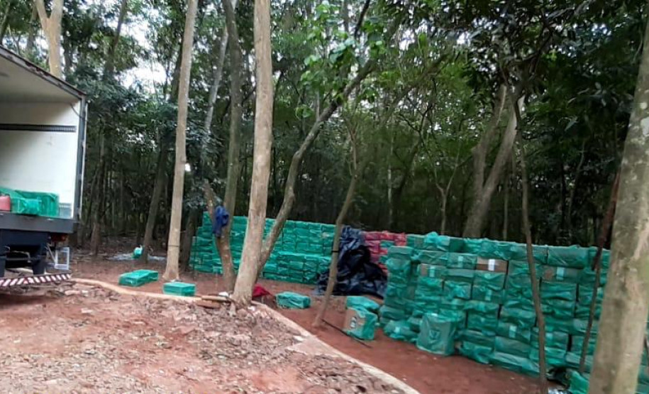 Centenas de tabletes de droga empilhados no chão, ao lado de caminhão