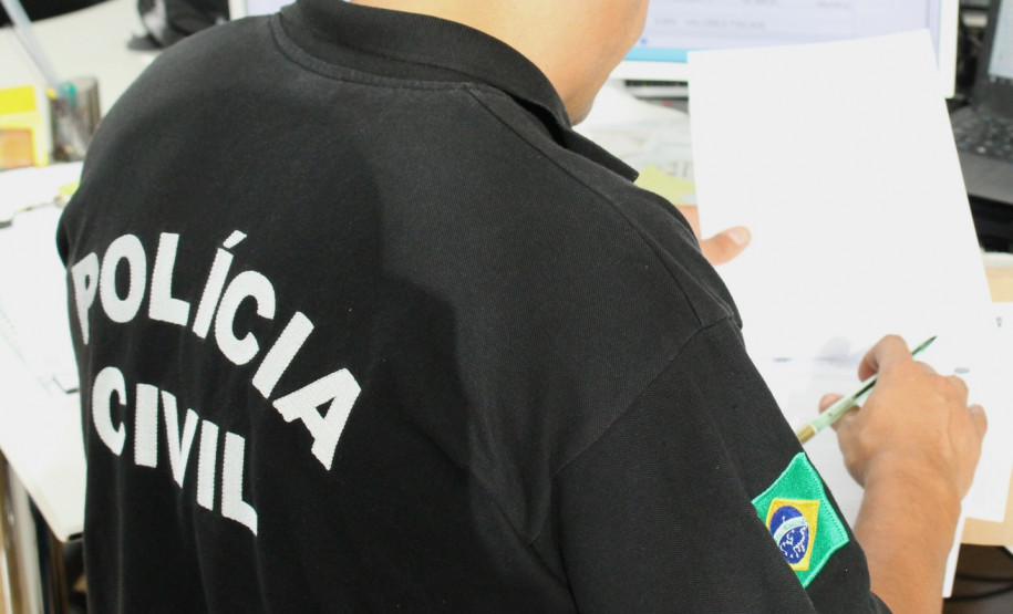 Policial civil sentado, de costas, averiguando documento