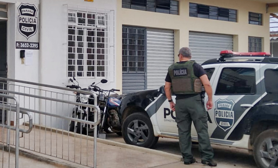 Policial civil ao lado de viatura, em frente a delegacia