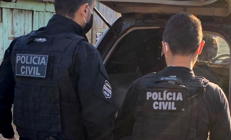 Dois policiais civis de costas, ao lado de viatura