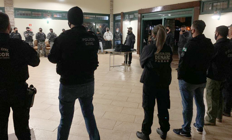 Policiais civis enfileirados, de costas