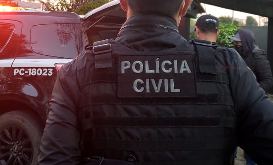 Policial civil de costas, próximo à viatura