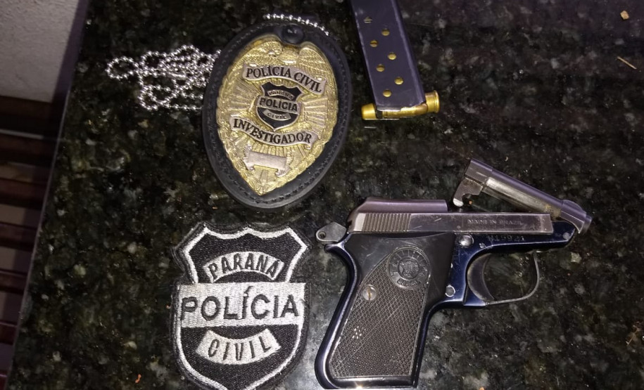Arma apreendida e distintivos da polícia, sobre uma mesa
