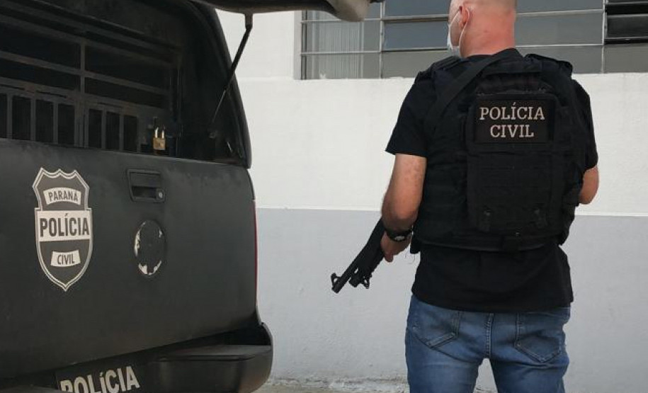Policial civil empunhando arma, ao lado de viatura