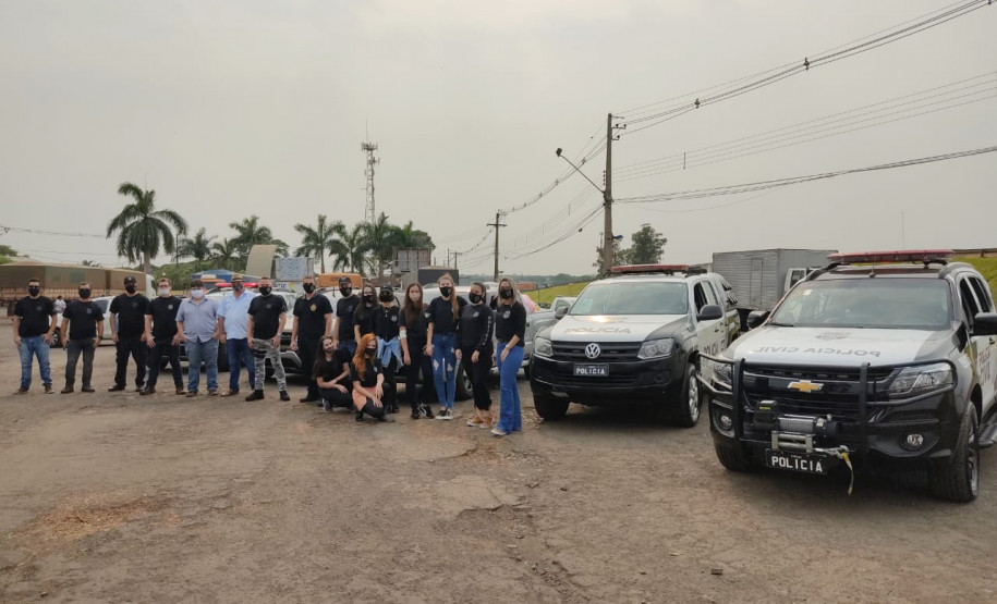 Policiais civis envolvidos no evento posando para foto ao lado de duas viaturas