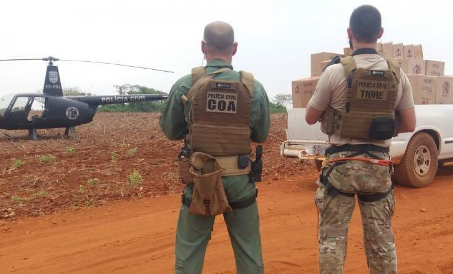 Policiais civis de costas, próximo veículo com contrabando e helicóptero da polícia