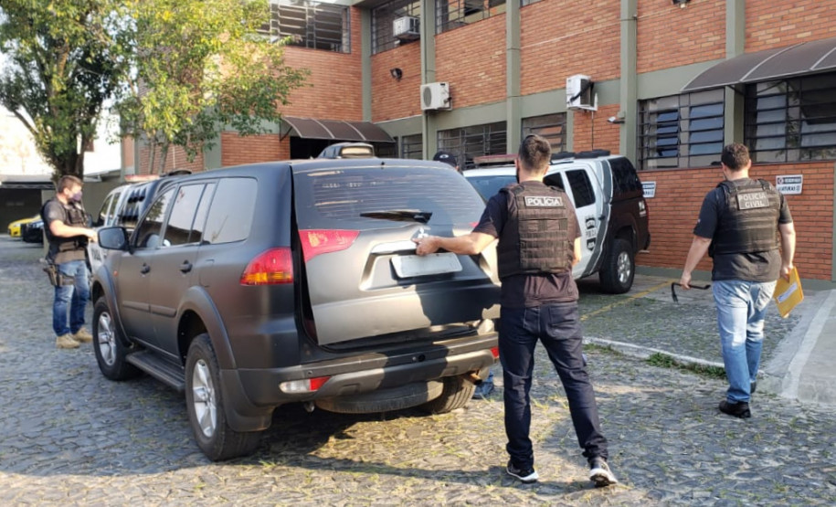 Trêspoliciais civis, um deles abrindo a tampa do porta-malas da viatura