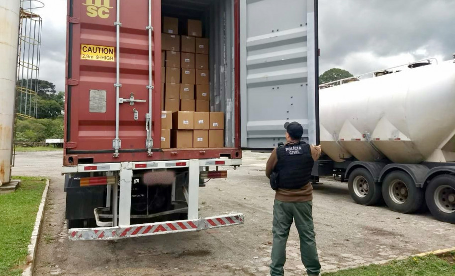 Policial civil segura porta do baú de caminhão e observa material recuperado