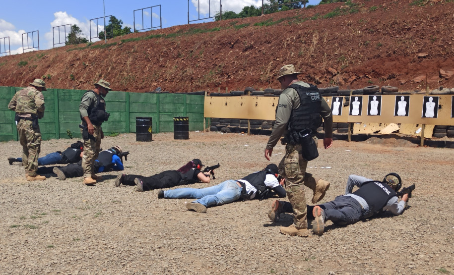 Policiais civis deitados, apontando as armas para alvos de papel, observados pelos instrutores