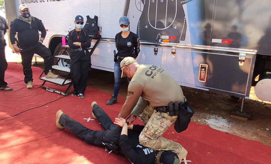 Policiais civis observam técnicas de algemamento, ao lado de caminhão simulador