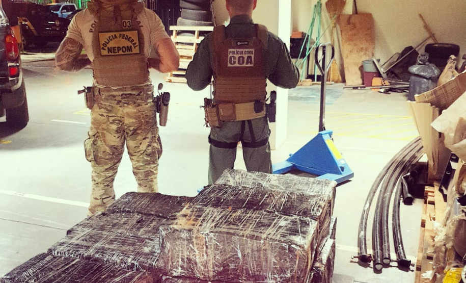 Dois policiais de costas. Em primeiro plano, pacotes com a droga