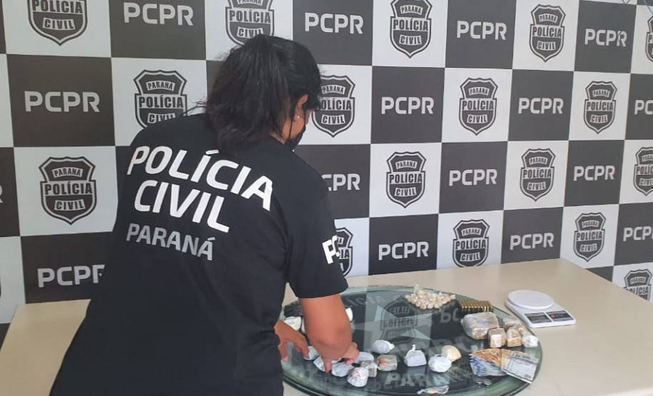 Policial civil de costas, reunindo material apreendido sobre uma mesa