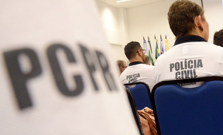 Policiais civis de costas, sentados. Em primeiro plano, nome PCPR