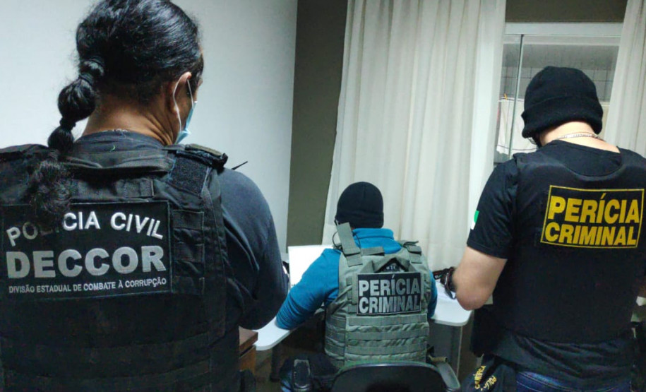 Três policiais civis de costas, analisando documentos