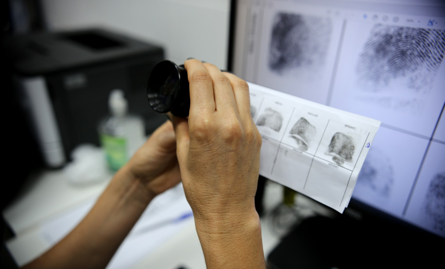 Foto mostra papiloscopista analisando digitais com lupa