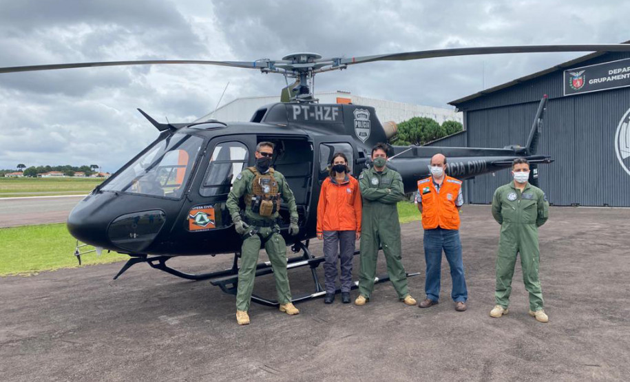 Policiais civis e membros da defesa civil posando para fotografia ao lado de helicóptero