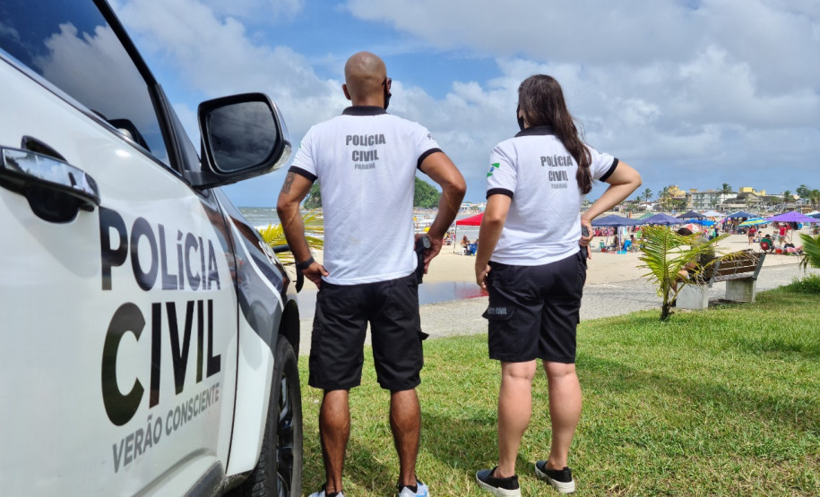 Dois policiais ao lado de viatura observam movimento no litoral
