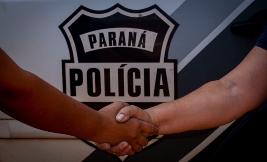 Policiais civis se cumprimentam em frente ao brasão da policia civil