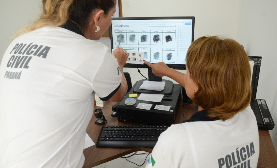 Duas policiais civis ao computador, analisando impressões digitais