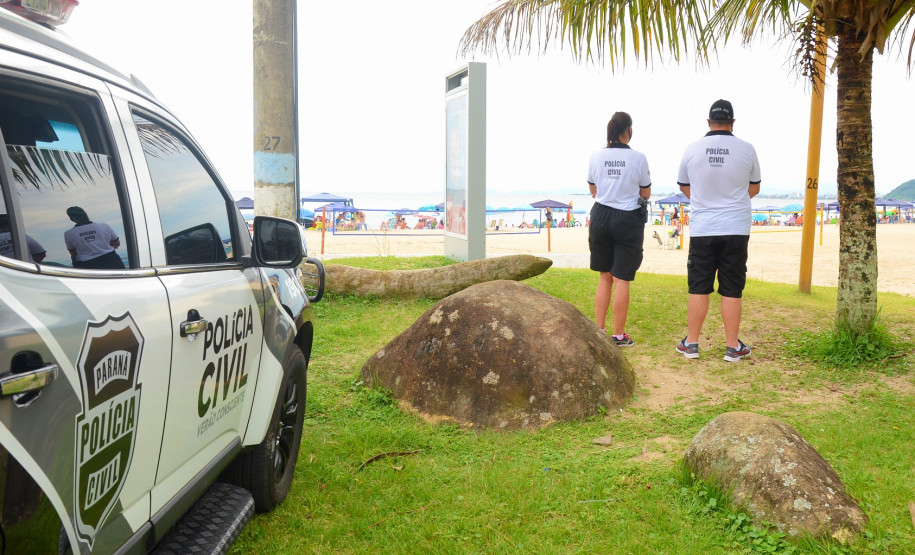 Dois policiais civis próximos a viatura, observando os veranistas