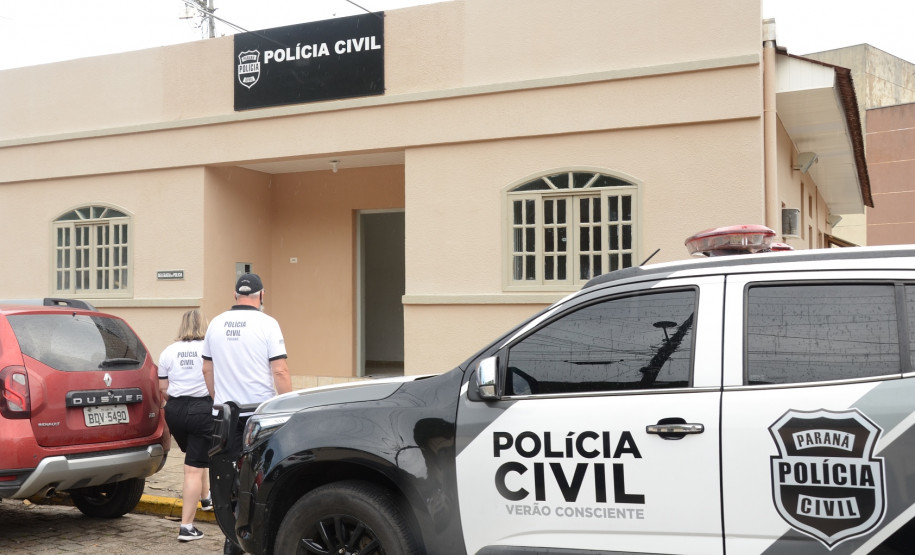 Dois policiais civis ao lado de viatura, entrando na delegacia de Guaratuba